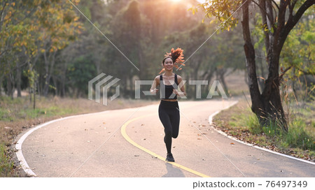 Young sporty woman running in the evening with sunset at the park. Young sporty woman running in the evening with sunset at the park. 76497349