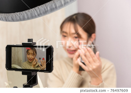 一個女人在她的智能手機上拍攝化妝視頻 76497609