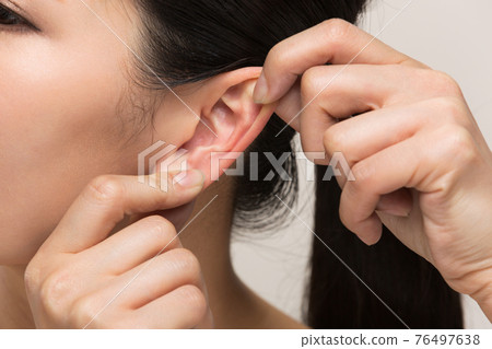 Woman massaging ears Woman massaging ears 76497638