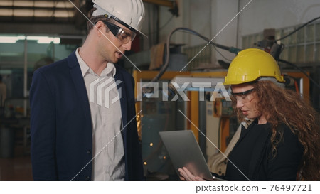 Two heavy industry business engineers in hardhats discuss information on laptop computer Two heavy industry business engineers in hardhats discuss information on laptop computer 76497721