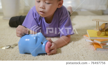 kid boy preschool putting pin money coins into blue faced piglet slot 76497756