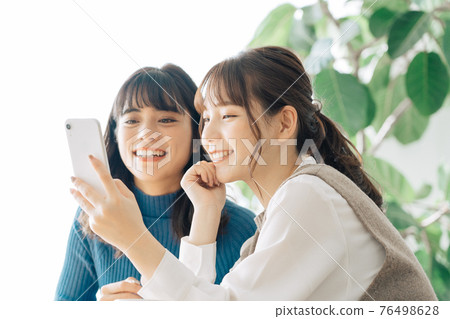 Two smiling women looking at a smartphone at a cafe Two smiling women looking at a smartphone at a cafe 76498628