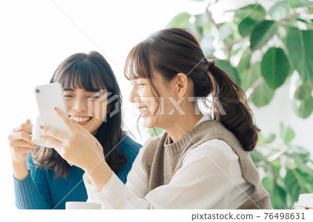Two smiling women looking at a smartphone at a cafe Two smiling women looking at a smartphone at a cafe 76498631