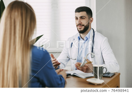 A serious male doctor of oriental appearance consults the patient, shows information about her illness and talks about the medical examination. 76498941