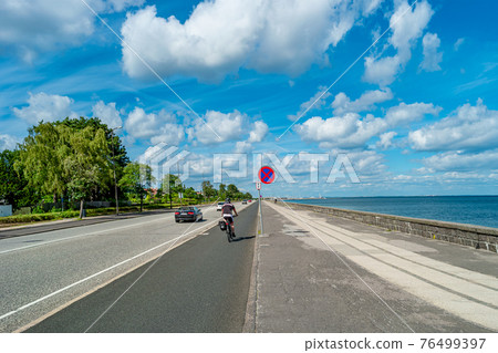 Cycling lane along sea bank and beach and lonely cyclist on bicycle in Copenhagen, Denmark Cycling lane along sea bank and beach and lonely cyclist on bicycle in Copenhagen, Denmark 76499397