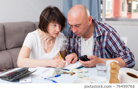 Mature couple with phone calculation money sitting at table 76499768