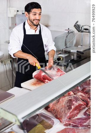 Adult butcher is cutting meat for seller to clients indoors. 76499929