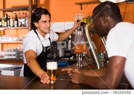 Smiling man barman giving glass of golden beer to client Smiling man barman giving glass of golden beer to client 76500508