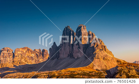 Panoramic view over beautiful sunset in magical Three Dolomite peaks at the national park Three Peaks (Tre Cime, Drei Zinnen) in Autumn October colors at blue sky, South Tyrol, Italy 76501426