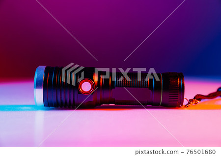 A small black flashlight in colored lighting. A small black flashlight in colored lighting. 76501680