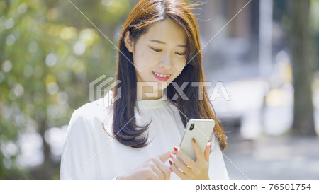 Woman operating a smartphone outdoors Woman operating a smartphone outdoors 76501754