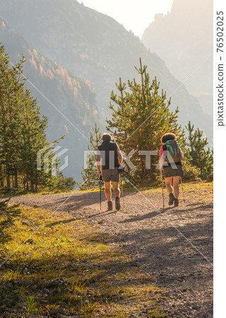 Two hikers at the trail in Dolomites at the national park Three Peaks (Tre Cime, Drei Zinnen) during sunset at direct light, South Tyrol, Italy, wide angle 76502025