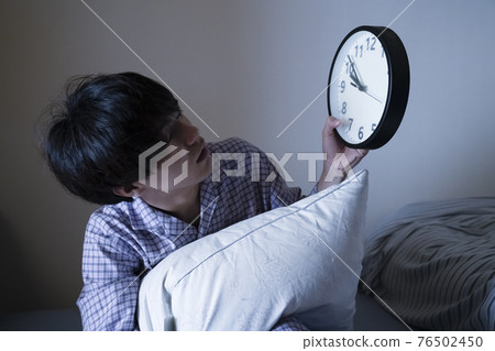 Man in pajamas looking at the clock 76502450