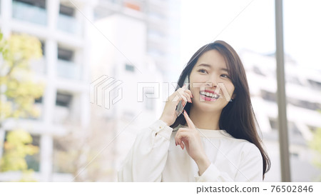 A woman talking on a smartphone while walking around the city 76502846