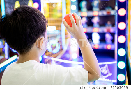 Kid boy playing a game of darts,holding a small plastic ball in his hands,aiming throwing at a target or a toy doll to knock it down,little child hurl the ball at the toys placed on the shelf to fall Kid boy playing a game of darts,holding a small plastic ball in his hands,aiming throwing at a target or a toy doll to knock it down,little child hurl the ball at the toys placed on the shelf to fall 76503699