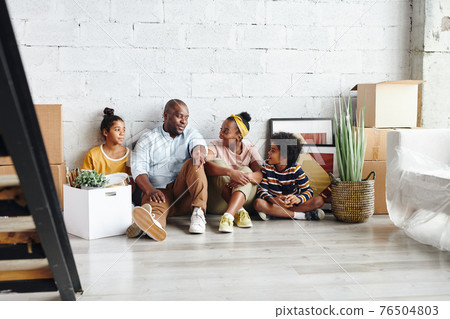 Contemporary African family of father, mother, little son and teenage daughter resting on the floor 76504803
