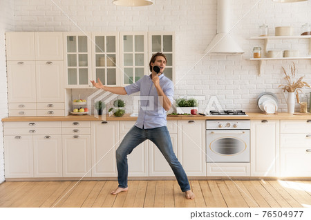 Funny man singing into kitchenware, dancing, having fun in kitchen 76504977