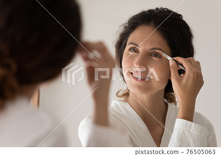 Close up smiling woman plucking thick eyebrows with tweezers 76505063