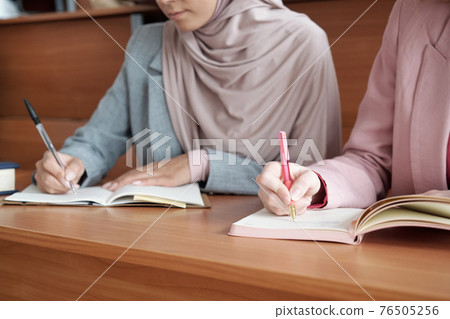 Hands of two young female students with pens making notes in copybooks at lecture 76505256