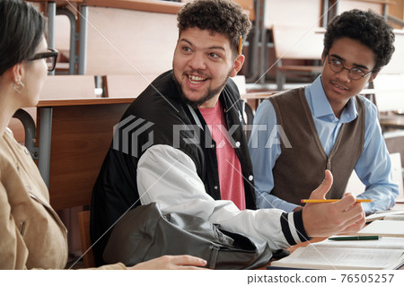 Happy guy with pencil looking at groupmate during discussion of project topic or passage from book Happy guy with pencil looking at groupmate during discussion of project topic or passage from book 76505257