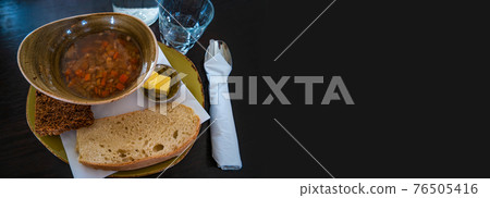 Banner with traditional Icelandic and Scandinavian lamb soup, white and brown bread, butter and spoon and glass of water at black background with copy space for text. Banner with traditional Icelandic and Scandinavian lamb soup, white and brown bread, butter and spoon and glass of water at black background with copy space for text. 76505416
