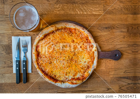 Delicious and appetizing fresh baked pizza margarita with cheese and tomato served with glass of beer and fork and knife with wooden background, details, closeup. Delicious and appetizing fresh baked pizza margarita with cheese and tomato served with glass of beer and fork and knife with wooden background, details, closeup. 76505471