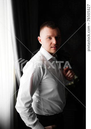 man in a white shirt by the window in a dark room. wedding day 76505827