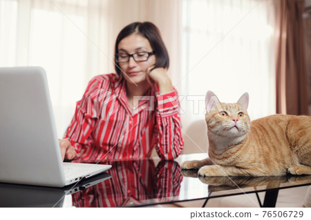 business woman in a red shirt with a ginger cat at home 76506729
