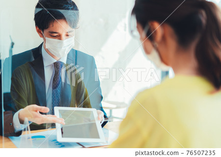 A man in a mask serving customers through an acrylic board A man in a mask serving customers through an acrylic board 76507235
