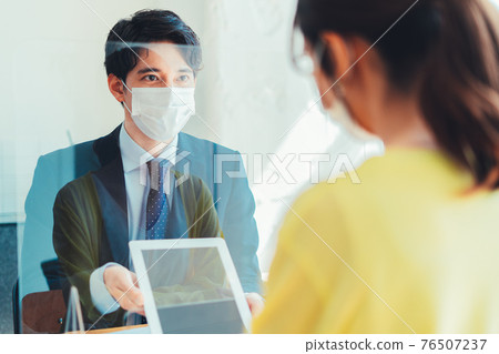 A man in a mask serving customers through an acrylic board A man in a mask serving customers through an acrylic board 76507237