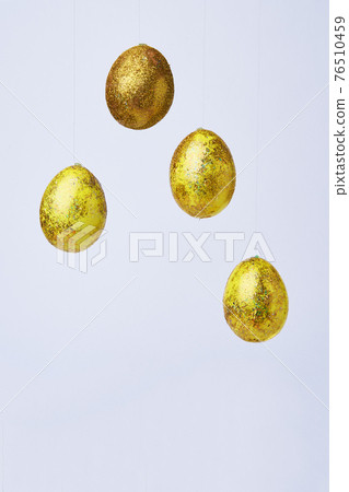 Golden shiny eggs hang on a white background. Golden shiny eggs hang on a white background. 76510459