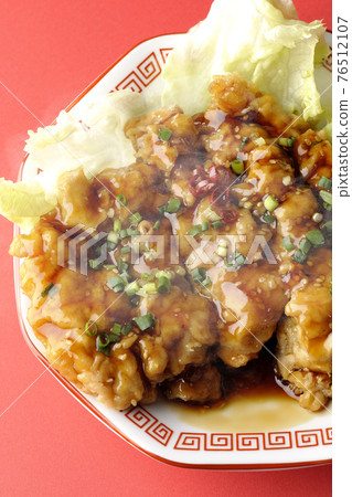 A photo of a hot oil sardine chicken with plenty of sauce and green onions on an octagonal plate against an appetizing red background (overhead view) 76512107