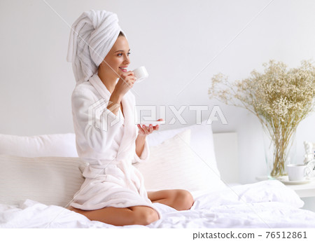 Happy young woman drinking coffee after shower Happy young woman drinking coffee after shower 76512861