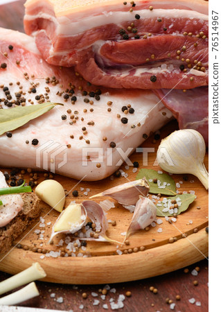 raw pork meat and lard with salt, spices and garlic on a cutting board, dark wooden background 76514967