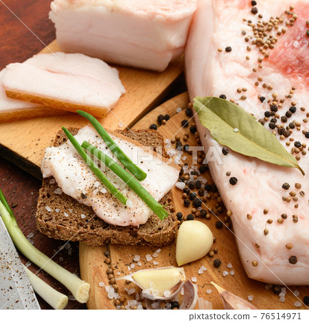 raw pork meat and lard with salt, spices and garlic on a cutting board, dark wooden background raw pork meat and lard with salt, spices and garlic on a cutting board, dark wooden background 76514971