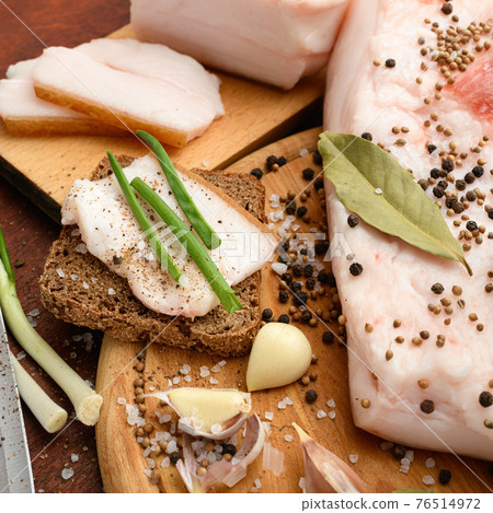 raw pork meat and lard with salt, spices and garlic on a cutting board, dark wooden background 76514972