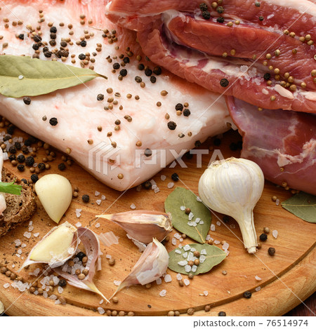 raw pork meat and lard with salt, spices and garlic on a cutting board, dark wooden background raw pork meat and lard with salt, spices and garlic on a cutting board, dark wooden background 76514974