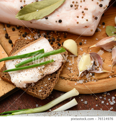 raw pork meat and lard with salt, spices and garlic on a cutting board, dark wooden background raw pork meat and lard with salt, spices and garlic on a cutting board, dark wooden background 76514976