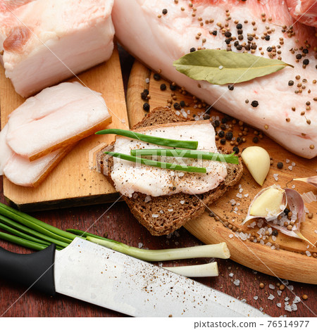 raw pork meat and lard with salt, spices and garlic on a cutting board, dark wooden background raw pork meat and lard with salt, spices and garlic on a cutting board, dark wooden background 76514977