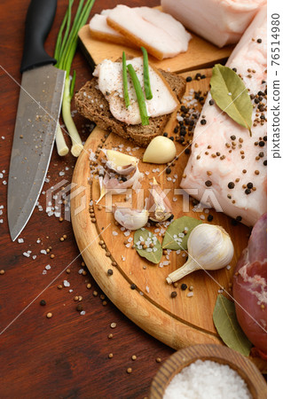raw pork meat and lard with salt, spices and garlic on a cutting board, dark wooden background 76514980