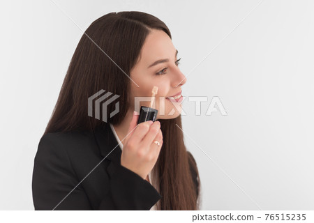 girl, makeup artist, with long dark hair in a business suit, applies a concealer on the face on a white background 76515235