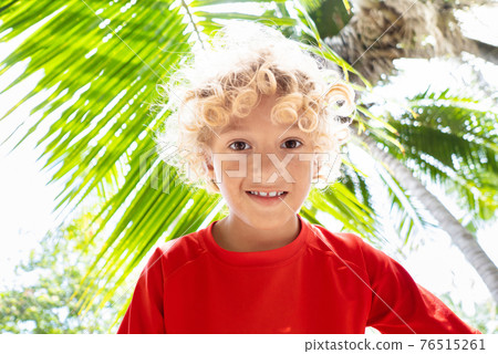 Beach fun. Curly boy under palm tree. 76515261