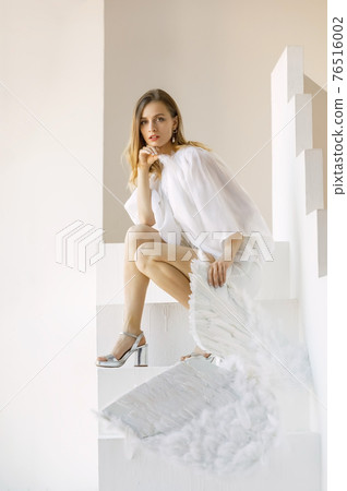 Beautiful young caucasian woman with angel wings poses in the studio Beautiful young caucasian woman with angel wings poses in the studio 76516002