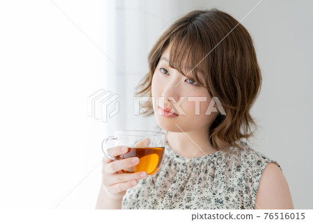 Young woman holding a cup of tea by the window Young woman holding a cup of tea by the window 76516015