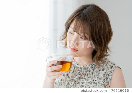 Young woman holding a cup of tea by the window 76516016