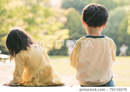 Back view of brother and sister sitting on the bench 76516070