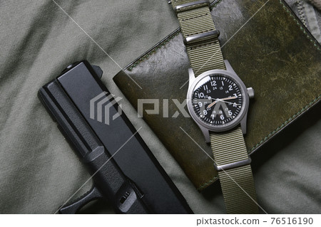 Vintage military watch with nato strap and pistol on army green background, Classic timepiece Vintage military watch with nato strap and pistol on army green background, Classic timepiece 76516190