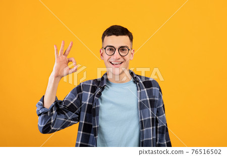 Portrait of happy millennial guy in glasses showing OK gesture over orange studio background Portrait of happy millennial guy in glasses showing OK gesture over orange studio background 76516502