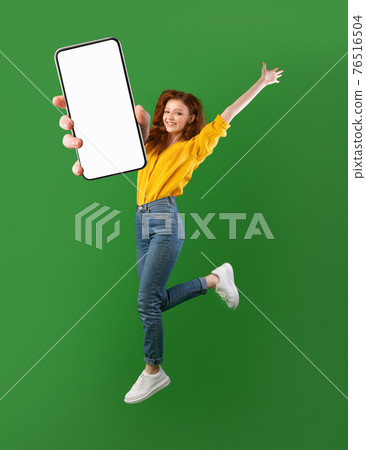 Hot offer, online sale. Carefree young woman jumping in air, showing cellphone with mockup space over green background Hot offer, online sale. Carefree young woman jumping in air, showing cellphone with mockup space over green background 76516504