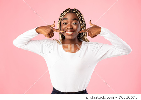 African american woman pointing forefingers at mouth and teeth African american woman pointing forefingers at mouth and teeth 76516573
